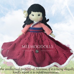 以下が含まれることがあります： 伝統的な韓国の韓服を着た手編みのドール。ドールは黒髪で、ピンクのトップス、青い帯、白い縁取りのある赤いスカートを着用しています。ドールはピンクの花畑に立っています。