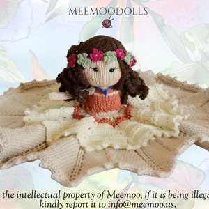Peut inclure: Une poup&eacute;e en tricot aux cheveux bruns portant une couronne de fleurs et une robe de couleur p&ecirc;che. La poup&eacute;e est assise sur une couverture en tricot beige avec une bordure en crochet blanc.