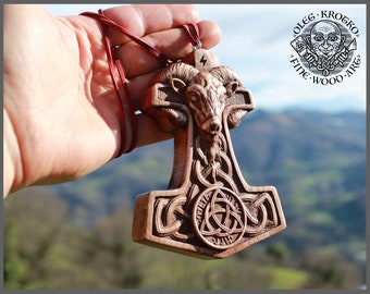 May include: A wooden pendant in the shape of Thor's hammer, Mjolnir, with a ram's head at the top and a Celtic knot design. The pendant is on a red cord and has the text "Fine Wood Art" on the back.