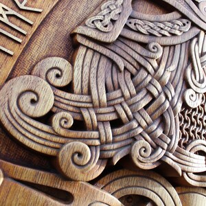 May include: A wooden carving of a Viking helmet with intricate knotwork and chainmail details. The helmet is surrounded by a border of runes, including the word "TIMR" which means "time".