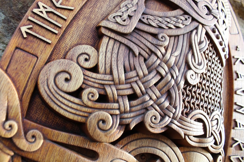 May include: A wooden carving of a Viking helmet with intricate knotwork and chainmail details. The helmet is surrounded by a border of runes, including the word "TIMR" which means "time".