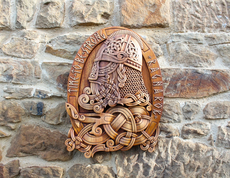 May include: A wooden carving of a Viking warrior's head with a horned helmet, surrounded by intricate knotwork. The carving is mounted on a wall and reads "TIME TO BE STRONG * RAGNAROK *"