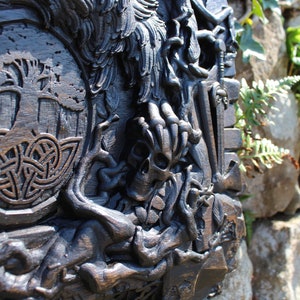 Puede incluir: Una talla de madera oscura de un &aacute;rbol de la vida con un dise&ntilde;o de nudo celta, una calavera y un p&aacute;jaro. La talla est&aacute; montada en una pared.