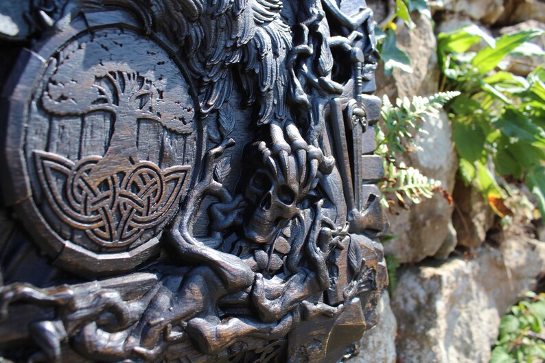 Puede incluir: Una talla de madera oscura de un &aacute;rbol de la vida con un dise&ntilde;o de nudo celta, una calavera y un p&aacute;jaro. La talla est&aacute; montada en una pared.