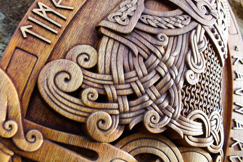 May include: A wooden carving of a Viking helmet with intricate knotwork and a chainmail design. The helmet is surrounded by a border of runes, which read "TIME".