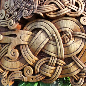 May include: A wooden carving of a knotwork design with intricate details. The carving is in shades of brown and gold, with a textured surface. The design includes a series of interlocking circles and spirals, creating a complex and visually appealing pattern.