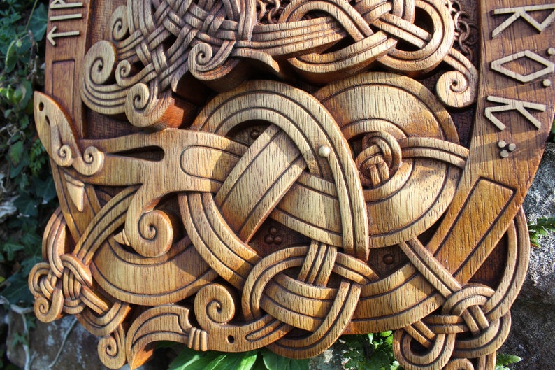 May include: A wooden carving of a knotwork design with intricate details. The carving is in shades of brown and gold, with a textured surface. The design includes a series of interlocking circles and spirals, creating a complex and visually appealing pattern.