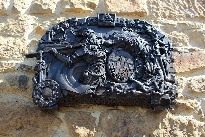 Puede incluir: Una talla de madera negra de un guerrero con un escudo y un lobo. La talla est&aacute; montada en una pared de piedra. El guerrero lleva armadura y un casco con alas. El lobo est&aacute; gru&ntilde;endo y muestra los dientes. El escudo tiene un dise&ntilde;o de nudo celta.