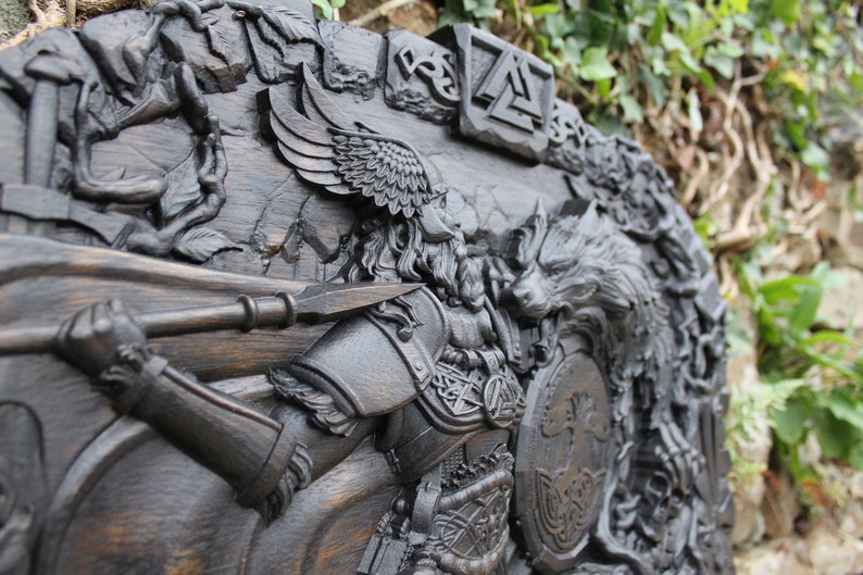 Puede incluir: Una talla de madera oscura de un guerrero con una lanza y un escudo, un lobo y un &aacute;rbol de la vida. La talla es detallada e intrincada, con un acabado de madera oscura.