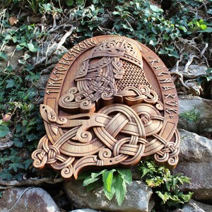 May include: A wooden carving of a Viking warrior's helmet with intricate knotwork and runes. The runes spell "Time to be strong" and "Ragnarok".