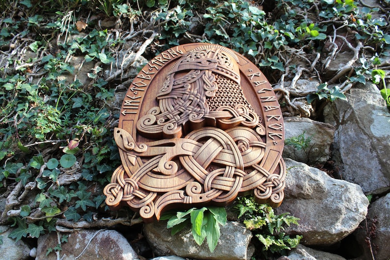 May include: A wooden carving of a Viking warrior's helmet with intricate knotwork and runes. The runes spell "Time to be strong" and "Ragnarok".