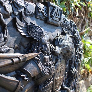 Puede incluir: Una talla de madera oscura de un guerrero vikingo con un lobo, un p&aacute;jaro y un escudo. La talla es detallada e intrincada, con una variedad de s&iacute;mbolos y dise&ntilde;os.