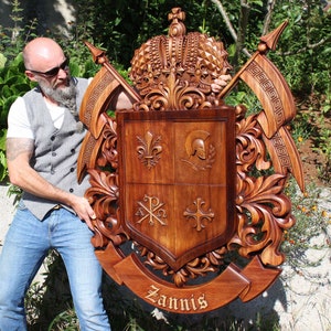 May include: A hand-carved wooden coat of arms with a crown, shield, and the name "Zannis" inscribed on a banner. The shield is divided into four sections, each with a different symbol. The coat of arms is a rich brown color and has intricate details.