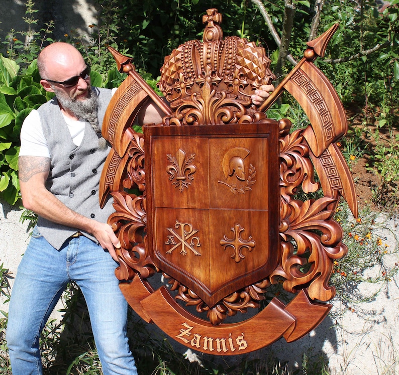 May include: A hand-carved wooden coat of arms with a crown, shield, and the name "Zannis" inscribed on a banner. The shield is divided into four sections, each with a different symbol. The coat of arms is a rich brown color and has intricate details.