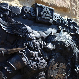 Puede incluir: Una talla de madera negra de un guerrero vikingo con un lobo, un escudo y un casco alado. La talla es detallada e intrincada, con una variedad de s&iacute;mbolos y dise&ntilde;os.