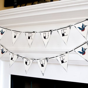 May include: A white banner with black string hangs above a fireplace. The banner spells out "TRUE LOVE" in black letters with a stylized bird design on each end.