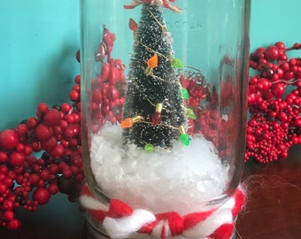 Christmas Tree Mason Jar Snowglobe, waterless decoration featuring tree covered in faux lights, nested in snow fluff, tied with chunky yarn