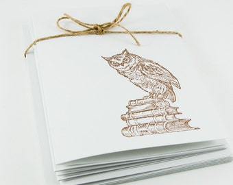 May include: A stack of blank white cards with a brown twine bow and a brown ink drawing of an owl perched on a stack of books.