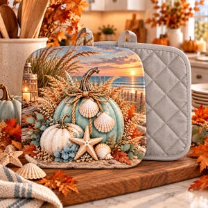 May include: A square quilted pot holder featuring a printed scene of two pumpkins, a starfish, and seashells arranged on a sandy beach. The background displays a sunset over the ocean with wheat stalks and a lantern. The reverse side is solid gray.