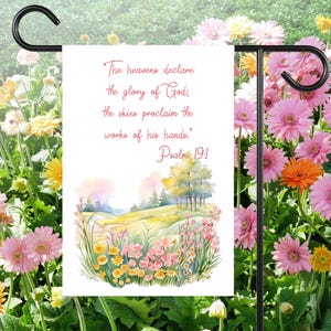 Könnte beinhalten: Eine weiße Gartenflagge mit einer Aquarell-Illustration eines Blumenfeldes und Bäumen. Der Text auf der Flagge lautet "The heavens declare the glory of God, the skies proclaim the works of his hands. Psalm 19:1"