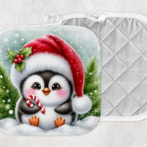 Puede incluir: Un par de agarraderas con temática navideña. Una presenta un lindo pingüino con un gorro de Papá Noel y un bastón de caramelo, en una escena nevada con árboles de hoja perenne. La otra es una agarradera blanca acolchada con un lazo para colgar.