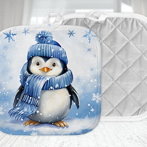 Puede incluir: Un agarrador de olla azul y blanco con un pingüino que lleva una bufanda y un gorro azules sobre un fondo nevado.