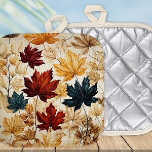 May include: A set of two pot holders with a quilted design. One pot holder features a white background with a quilted design. The other pot holder features a cream background with a pattern of colorful maple leaves.