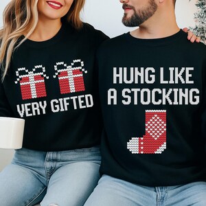 May include: Black sweatshirts with holiday-themed designs. One sweatshirt says "VERY GIFTED" with two red gift boxes. The other says "HUNG LIKE A STOCKING" with a red and white stocking graphic. Both have white text.