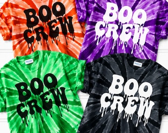 May include: Four short-sleeve t-shirts in orange, purple, green, and black tie-dye patterns. Each shirt features the text "BOO CREW" in a dripping, melted font style. The orange and green shirts have black text, while the purple and black shirts have white text.
