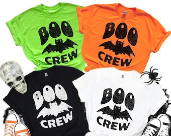 May include: Four short-sleeved t-shirts in neon green, orange, black, and white, each featuring a distressed graphic with the text "BOO CREW" and a bat illustration. Halloween-themed apparel.