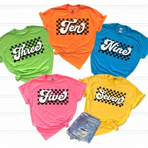 May include: Five colourful t-shirts with a black and white chequered pattern and a white number in a retro font. The numbers on the shirts are three, five, seven, nine, and ten.