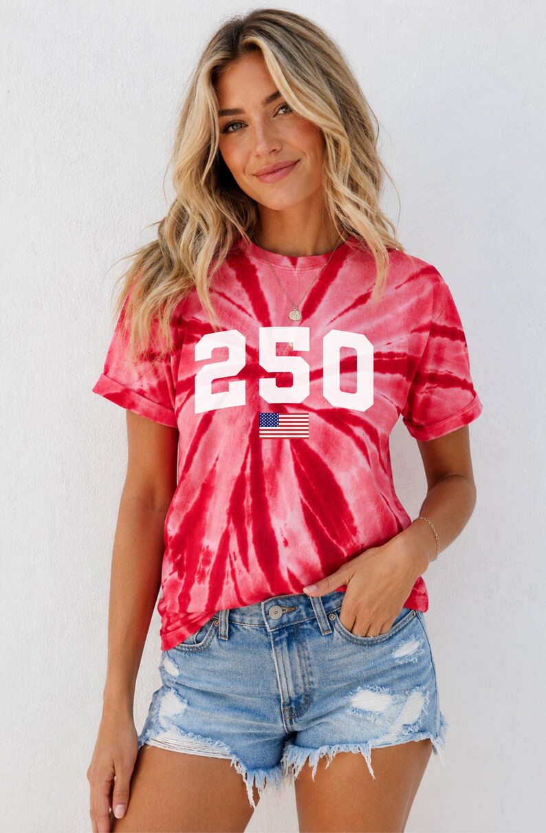 May include: Red tie-dye t-shirt featuring the number "250" in white and a small American flag graphic. The shirt is worn with denim shorts. The style is casual and summery.