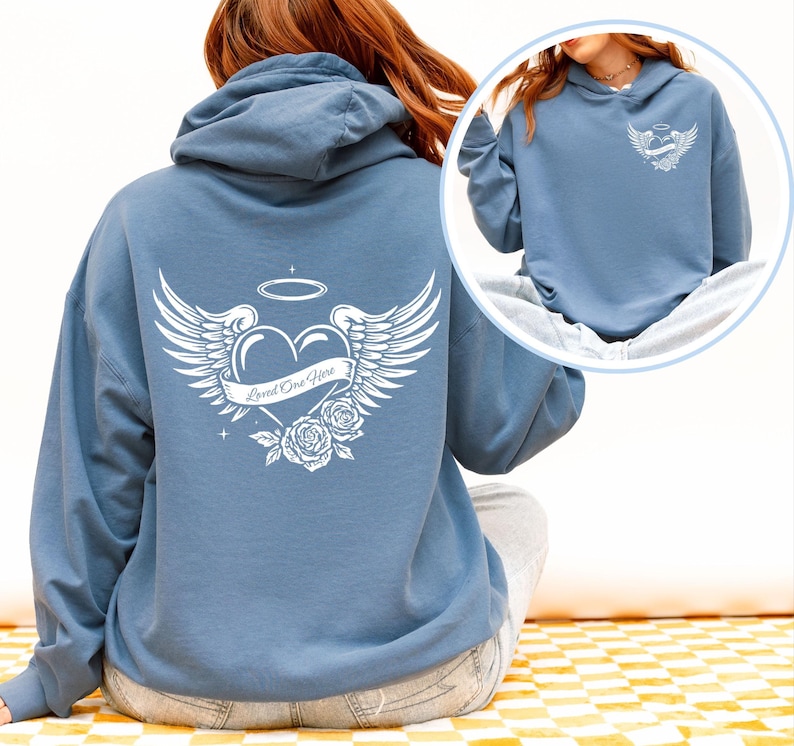 May include: A blue hoodie with a white graphic on the back featuring a heart with wings, a halo, roses, and the text "Loved One Here". The hoodie has a drawstring hood and long sleeves.