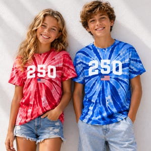 May include: Two people wearing matching tie-dye t-shirts. One shirt is red and the other is blue. Each shirt has the number "250" printed on the front in white, with a small American flag underneath. The shirts are short-sleeved.