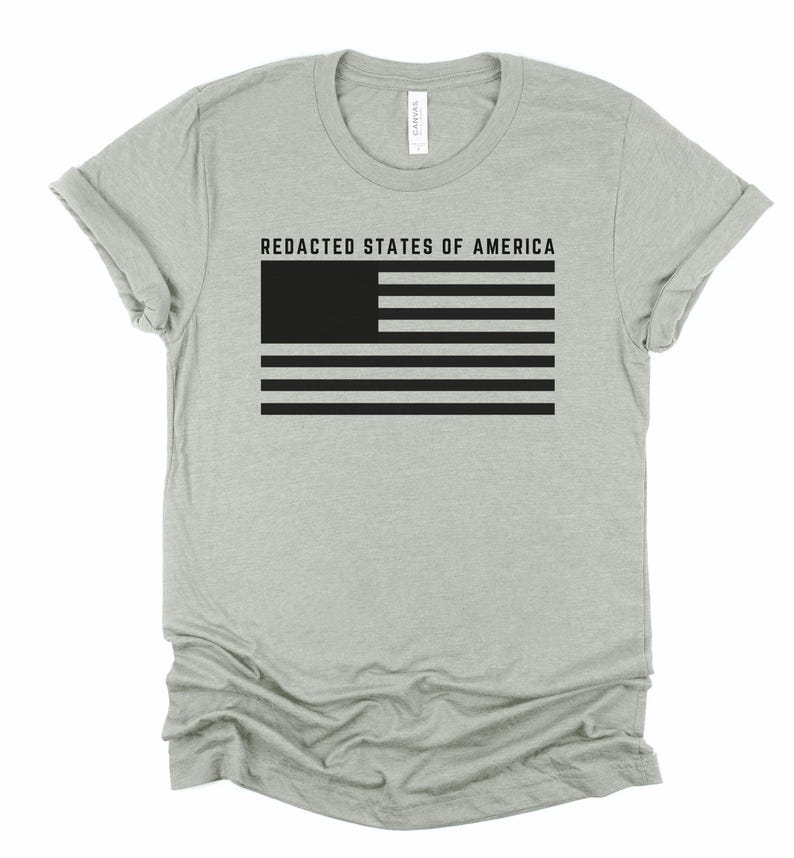 K&ouml;nnte beinhalten: Hellgraues T-Shirt mit dem Text "REDACTED STATES OF AMERICA" &uuml;ber einem schwarz-wei&szlig;en Flaggen-Design. Die Flagge hat ein schwarzes Rechteck in der oberen linken Ecke und schwarze Streifen.