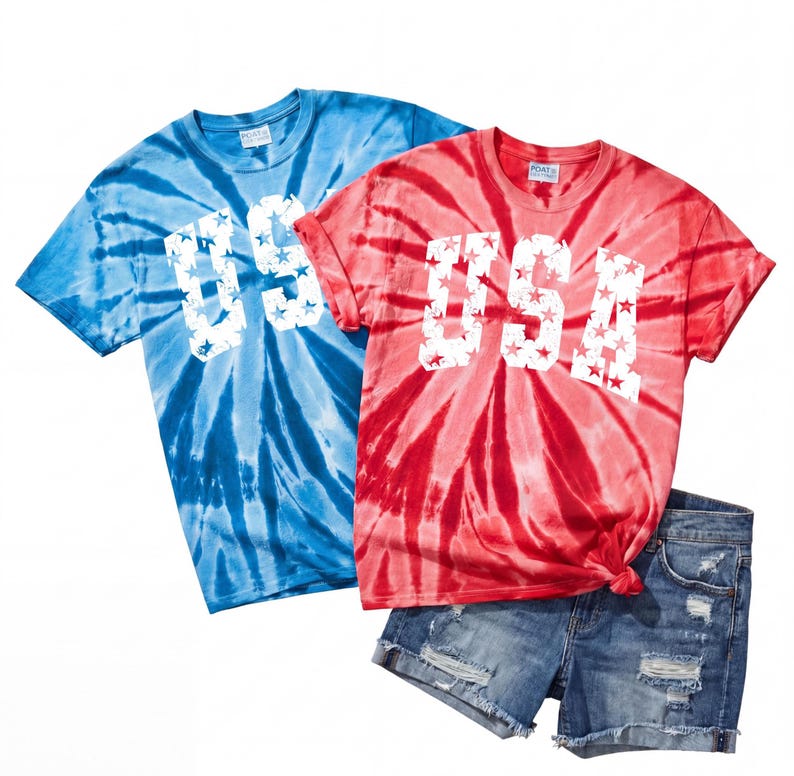 May include: Two tie-dye t-shirts, one blue and one red, with the word "USA" in white, star-filled letters. The shirts are paired with denim shorts. The shirts have a spiral pattern.
