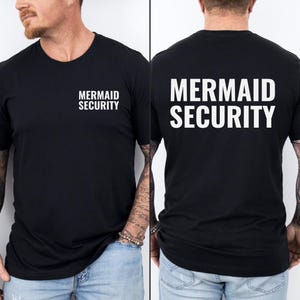 Może przedstawiać: Czarny T-shirt z białym napisem "Mermaid Security" z przodu i z tyłu.