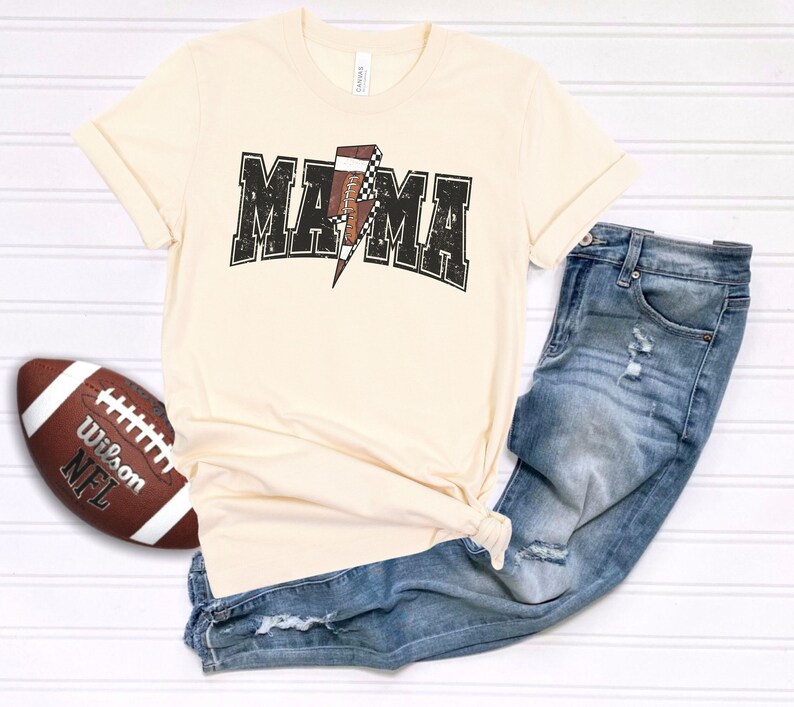 May include: A beige t-shirt with a black and white checkered football graphic and the text "MAMA" in a black distressed font.