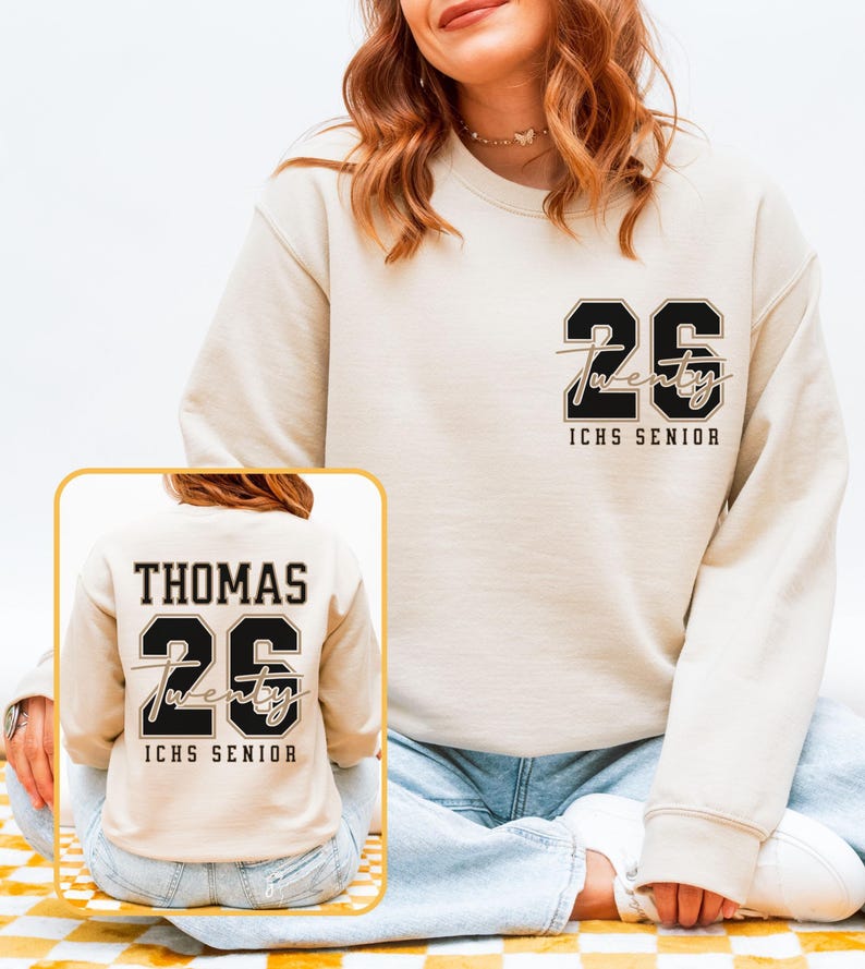 May include: A cream-colored sweatshirt with the number "26" in black and the word "twenty" in cursive. The text "ICHS SENIOR" is below the number. A smaller image shows the back of the sweatshirt with the name "THOMAS" above the number.