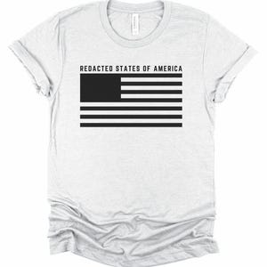 K&ouml;nnte beinhalten: Hellgraues T-Shirt mit dem Text "REDACTED STATES OF AMERICA" &uuml;ber einem schwarz-wei&szlig;en Flaggen-Design. Das Shirt besteht aus einem weichen Material und hat einen Rundhalsausschnitt.
