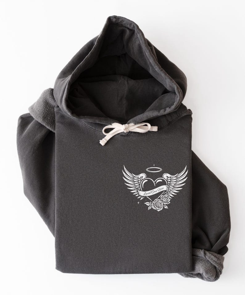 May include: Dark gray hoodie with a white drawstring and a white graphic on the chest. The graphic features a heart with wings, a halo, and the words "Loved One Here" on a banner, with roses below.
