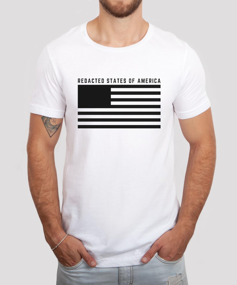 K&ouml;nnte beinhalten: Wei&szlig;es T-Shirt mit dem Text "REDACTED STATES OF AMERICA" &uuml;ber einem schwarz-wei&szlig;en Flaggen-Design. Die Flagge hat ein schwarzes Rechteck in der oberen linken Ecke und abwechselnd schwarze und wei&szlig;e Streifen.