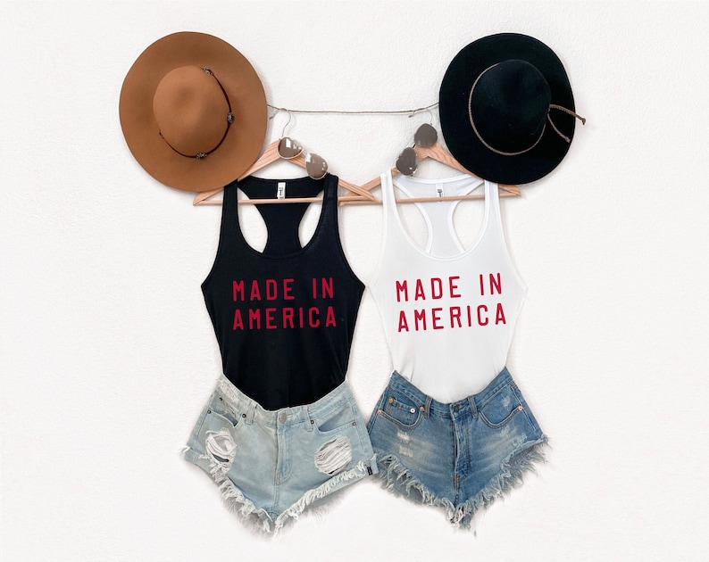 K&ouml;nnte beinhalten: Zwei Tanktops mit dem Text "Made in America" in roten Buchstaben. Ein Tanktop ist schwarz und das andere wei&szlig;. Beide Tanktops h&auml;ngen an einer W&auml;scheleine mit H&uuml;ten und Sonnenbrillen.
