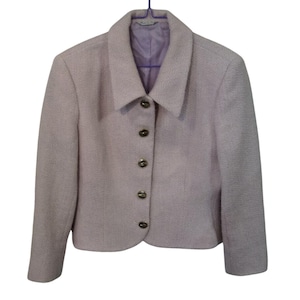 May include: A light lavender blazer with a textured fabric finish, featuring a pointed collar, long sleeves, and a front closure with five round, metallic-toned buttons. The interior is lined with a smooth, matching light lavender fabric.