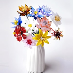 May include: A bouquet of colorful glass flowers in a white vase. The flowers are various colors, including red, yellow, blue, and orange. The vase has the text "I STAY IN LOVE" and "handmade with love" at the bottom.