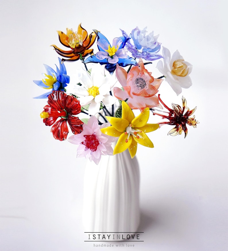May include: A bouquet of colorful glass flowers in a white vase. The flowers are various colors, including red, yellow, blue, and orange. The vase has the text "I STAY IN LOVE" and "handmade with love" at the bottom.