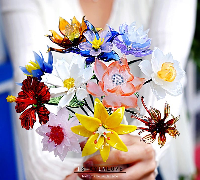 May include: A vibrant bouquet of handmade glass flowers in a variety of colours, including red, yellow, orange, blue, and white. The flowers are arranged together, creating a colourful display. The text "I STAY IN LOVE" is visible at the bottom.