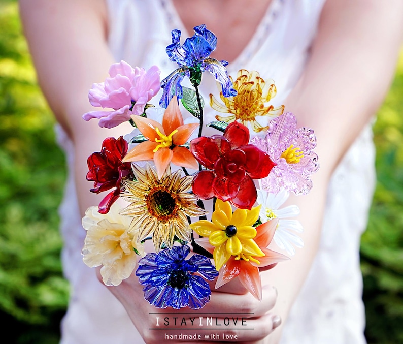 May include: A colorful bouquet of glass flowers in shades of red, orange, yellow, blue, and pink. The flowers are held in a person's hands. The text "I STAY IN LOVE" and "handmade with love" is at the bottom of the image.