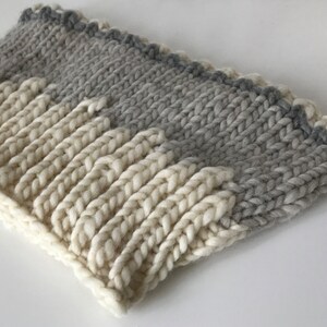 May include: A knitted headband with a white and gray ombre design. The headband is made of a soft, chunky yarn.