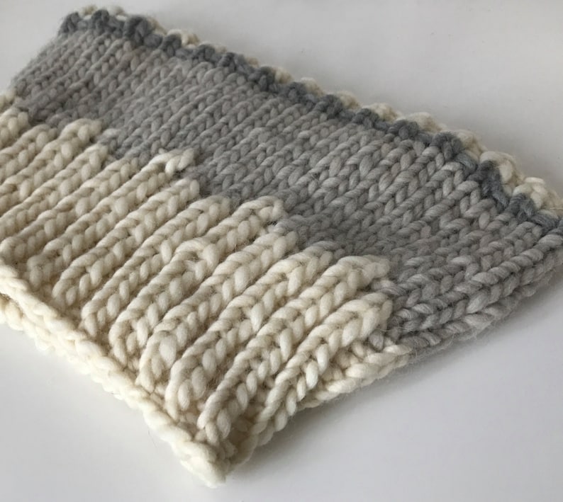 May include: A knitted headband with a white and gray ombre design. The headband is made of a soft, chunky yarn.